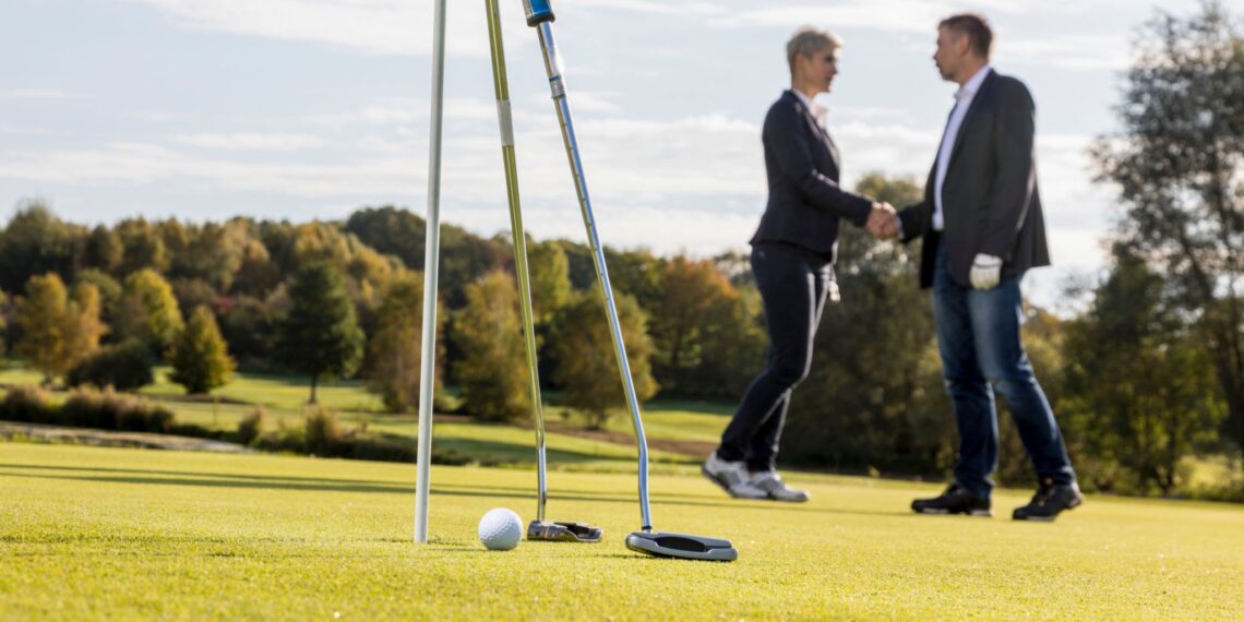 two persons playing golf dressed in buisness suits shaking hands at the end of a game